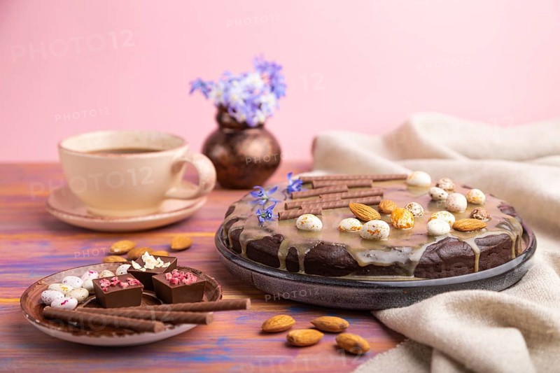 Homemade chocolate brownie cake with caramel cream and almonds with cup of coffee on a colored and pink background and linen textile. Side view, close up, selective focus