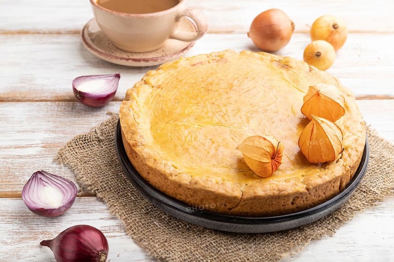 Autumn onion pie and cup of coffee on white wooden background and linen textile. Side view, close up