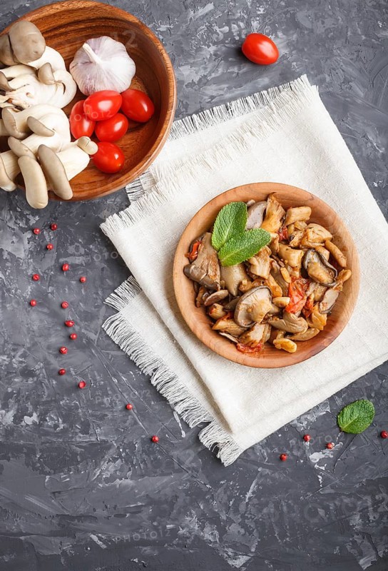 Fried oyster mushrooms with tomatoes in wooden plate on black concrete background. top view, copy space