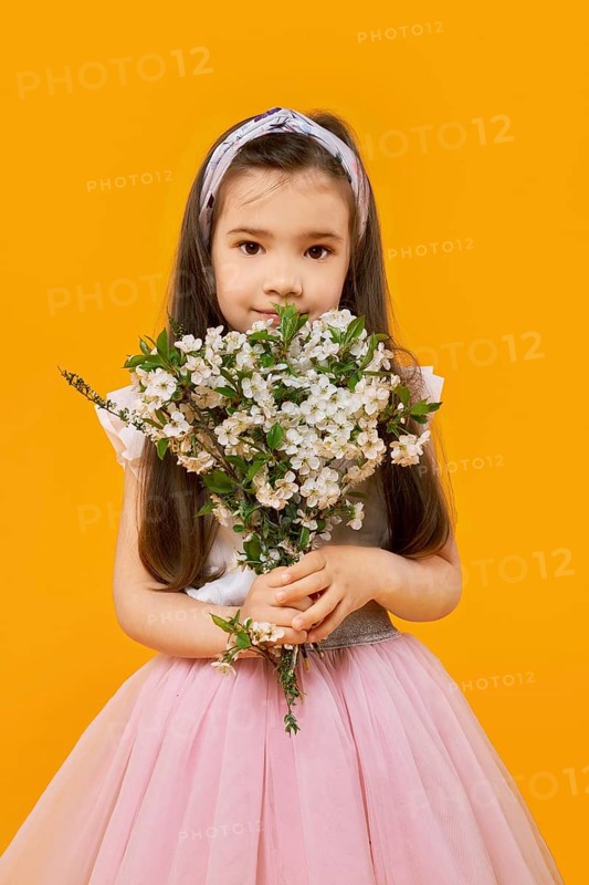 Cute young girl with bouquet of spring flowers over yellow background