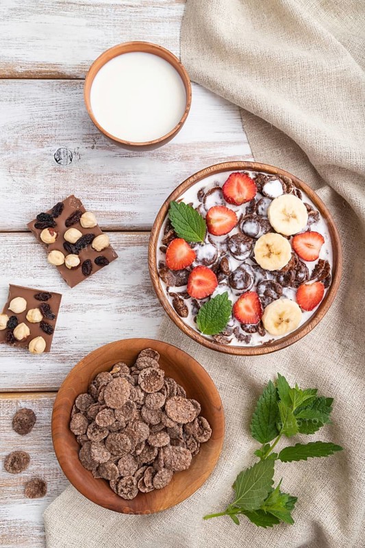 Chocolate cornflakes with milk and strawberry in wooden bowl on white wooden background and linen textile. Top view, flat lay, close up