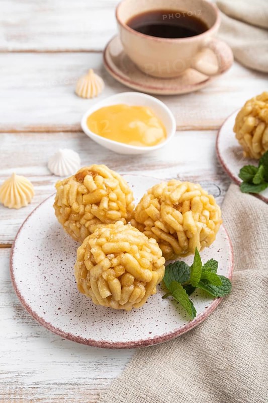 Traditional Tatar candy chak-chak made of dough and honey with cup of coffee on a white wooden background and linen textile. Side view, close up