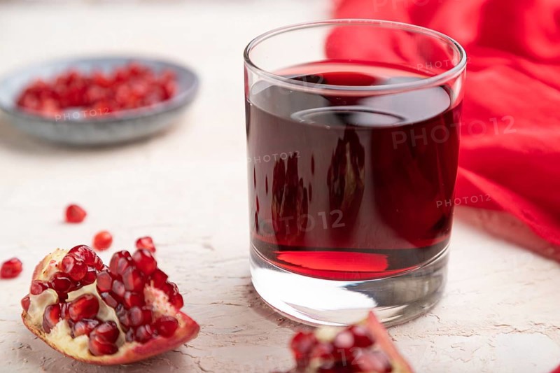 Glass of pomegranate juice on a white concrete background with red textile. Side view, close up, selective focus