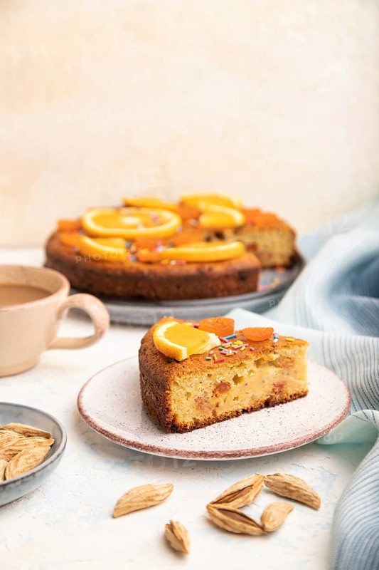 Orange cake with almonds and a cup of coffee on a white concrete background and blue linen textile. Top view, close up, selective focus