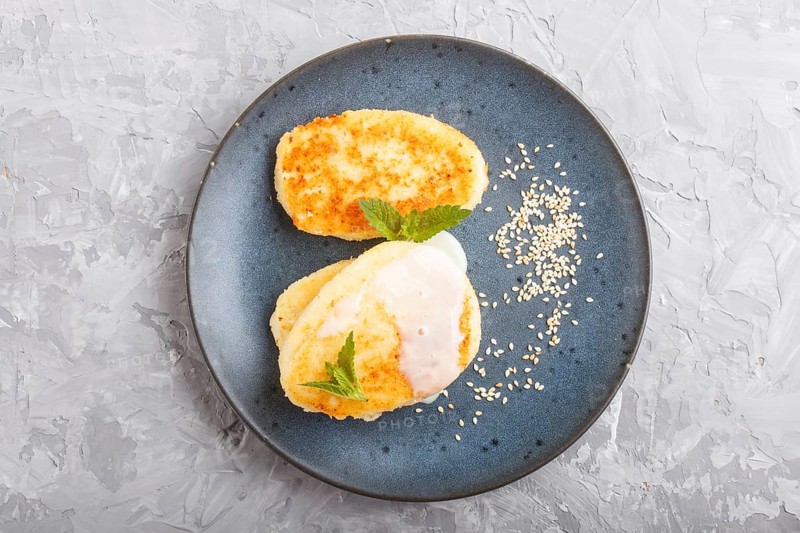 Cheese pancakes on a blue ceramic plate with milk sauce on a gray concrete background. top view, flat lay