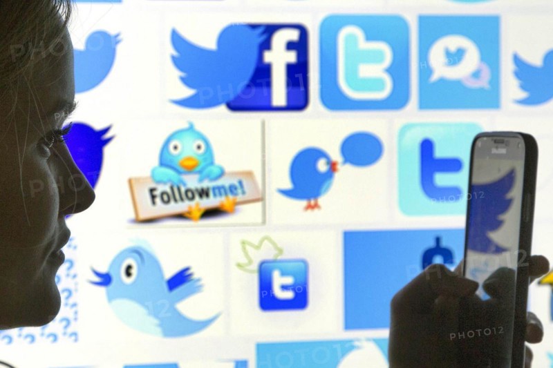 Silhouette of a woman with a smartphone in her hand in front of a Facebook and Twitter logo, 12/01/2016