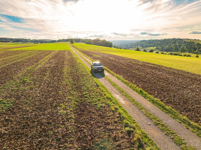 A car drives along a rural road, surrounded by expansive fields under bright daylight, car sharing, VW ID5, Calw, Black Forest, Germany, Europe