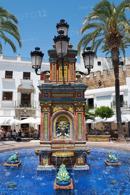 Decorative fountain with ceramic details and four lanterns, surrounded by palm trees, in warm Mediterranean style, fountain with azulejos, Plaza de España, square, old town centre, Vejer de la Frontera, province of Cádiz, Cadiz, Andalusia, Spain, Europe