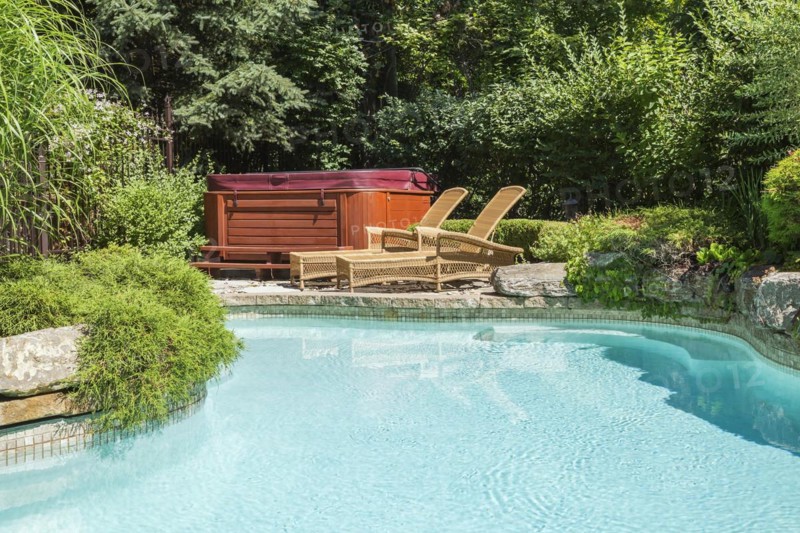 In-ground swimming pool surrounded by copper coloured wrought iron metal security fence and various perennial plants, shrubs and trees in residential backyard of luxurious home, Quebec, Canada, North America