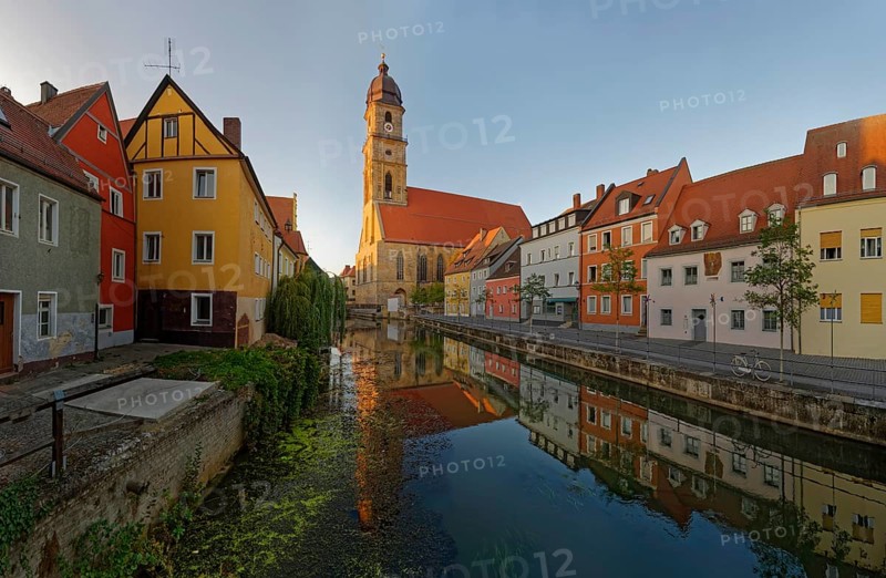 The morning sun illuminates a picturesque street along the river Vils and the church tower of St Martin's Basilica, Amberg, Upper Palatinate, Bavaria, Germany, Europe
