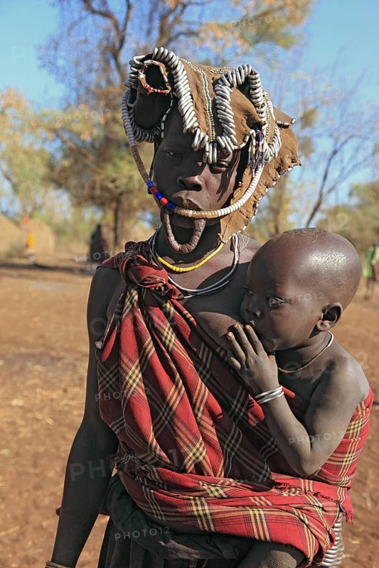 South Ethiopia, in Maco National Park, Mursi tribe, Mursi woman with baby, painted skin and headdress, baby drinking from breast, plate-lipped woman without plate, Ethiopia, Africa