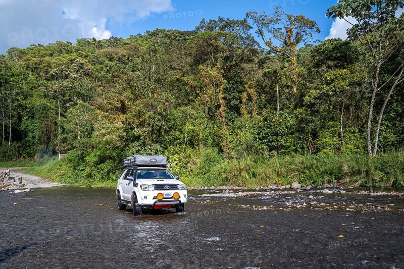 Toyota off-road vehicle with roof tent drives through a wide river in the rainforest, Alajuela province, Costa Rica, Central America