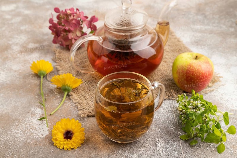 Red tea with herbs in glass teapot on brown concrete background and linen textile. Healthy drink concept. Side view, close up