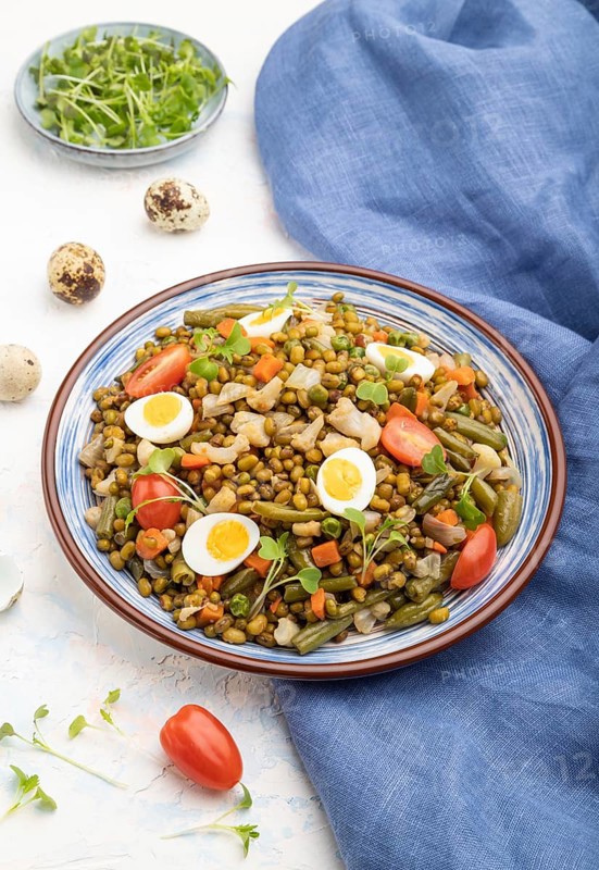 Mung bean porridge with quail eggs, tomatoes and microgreen sprouts on a white concrete background and blue textile. Side view, close up
