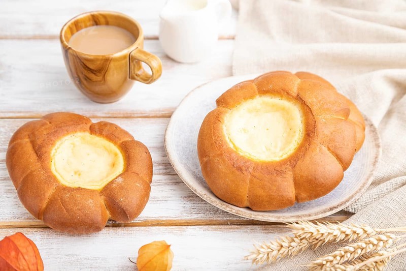 Sour cream bun with cup of coffee on a white wooden background and linen textile. Side view, close up, selective focus