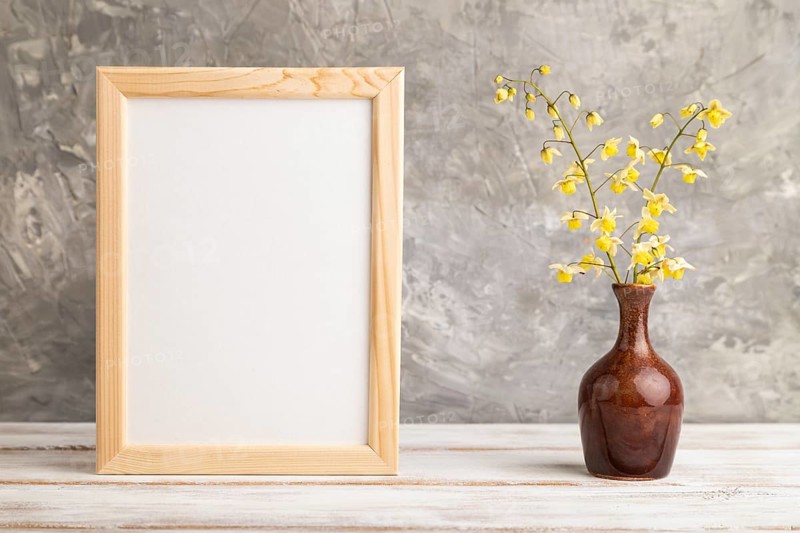 Wooden frame with yellow barrenwort flowers in ceramic vase on gray concrete background. side view, copy space, still life, mockup, template, spring, summer minimalism concept