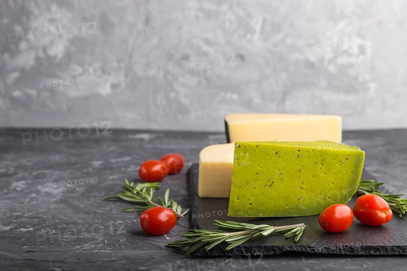 Green basil cheese and various types of cheese with rosemary and tomatoes on black slate board on a black concrete background. Side view, close up, copy space, selective focus