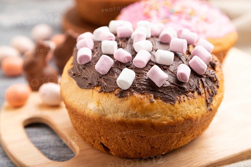 Homemade glazed and decorated easter pies with chocolate eggs and rabbits on a gray wooden background and linen textile. Side view, selective focus, close up