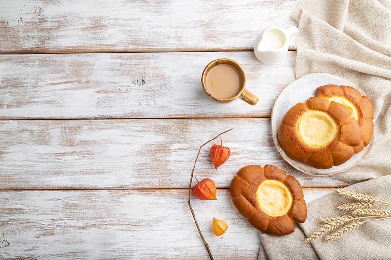 Sour cream bun with cup of coffee on a white wooden background and linen textile. top view, flat lay, copy space