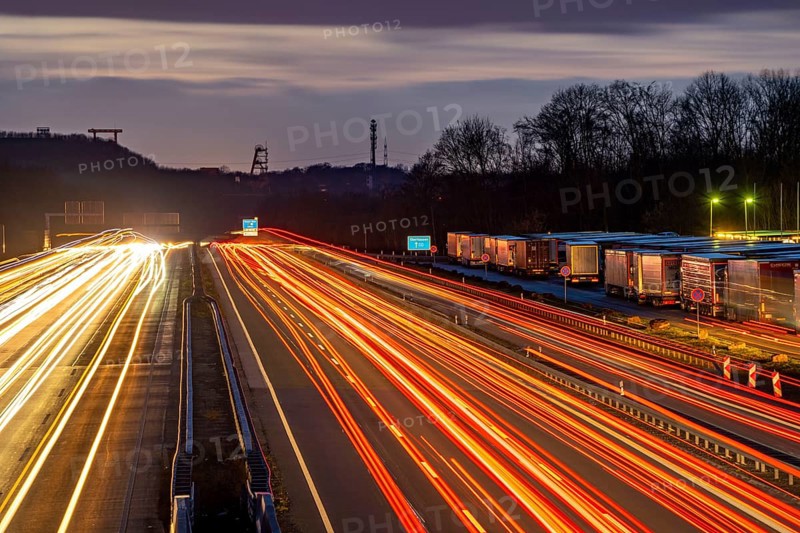 Evening traffic on the A2 motorway at the Recklinghausen junction heading west, in the background the headframes of the former Ewald colliery, Hohenhorst rest area, overflowing with lorries, North Rhine-Westphalia, Germany, Europe