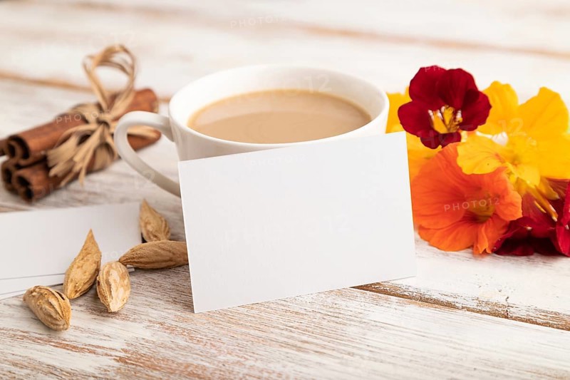 White paper business card mockup with orange nasturtium flower and cup of coffee on white wooden background. Blank, side view, copy space, still life. spring concept
