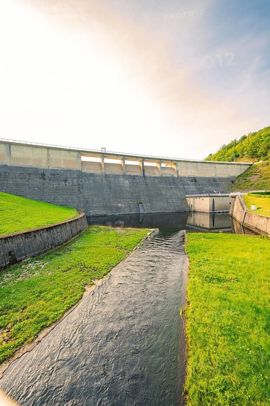 A river flowing under a large concrete dam, surrounded by grass and nature, Rappbode Dam, Harz Mountains, Germany, Europe