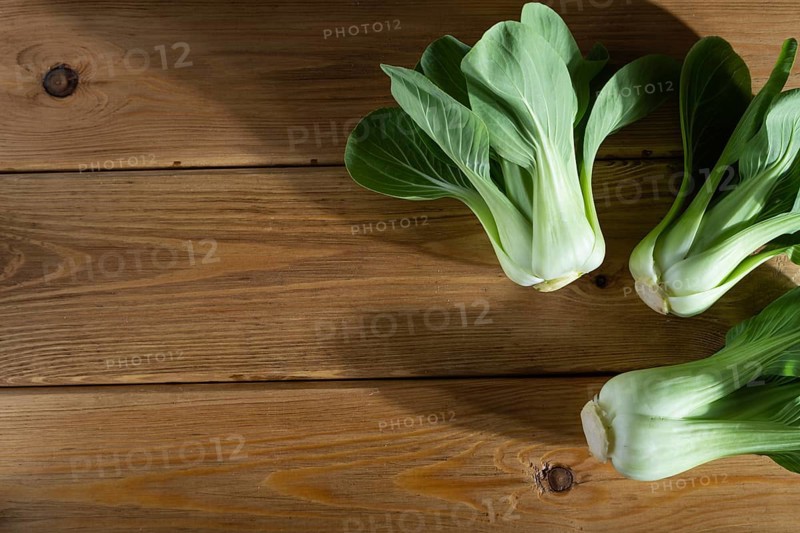 Fresh green bok choy or pac choi chinese cabbage on a brown wooden background. Hard light, contrast. Top view, copy space, flat lay