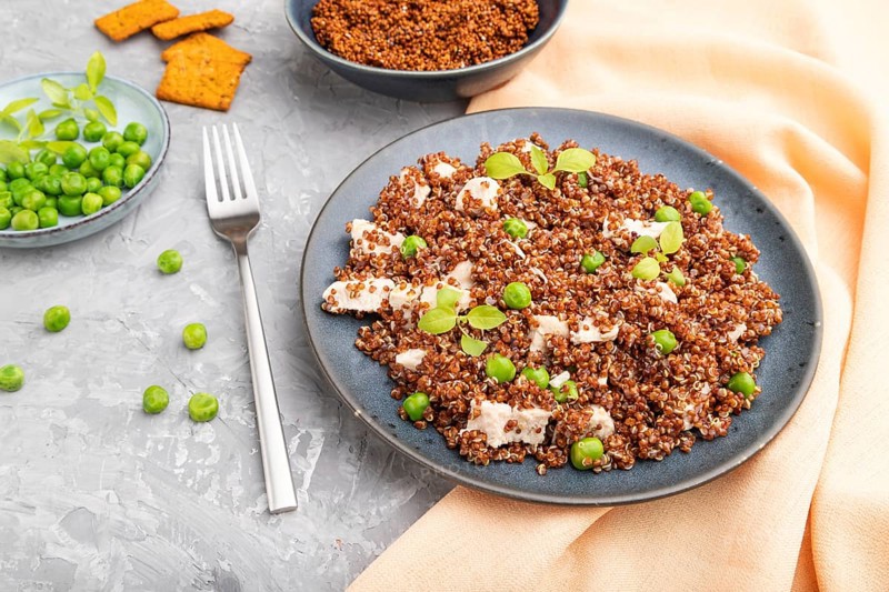 Quinoa porridge with green pea and chicken on ceramic plate on a gray concrete background and orange textile. Side view, close up