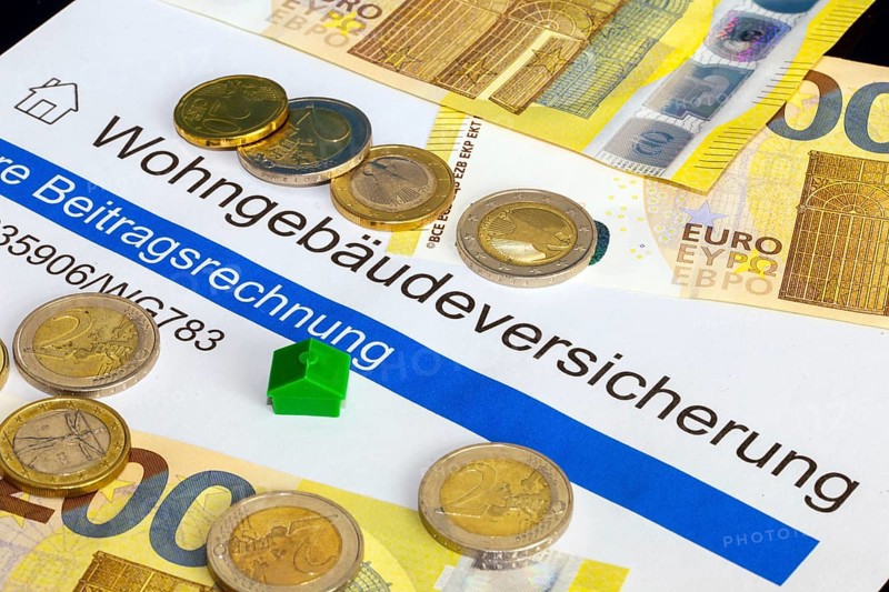 Symbolic image of building insurance: close-up of contract documents, a model house, euro banknotes and euro coins