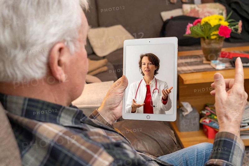 Symbolic image of telemedicine, elderly patient speaking to a doctor in a video conference from home