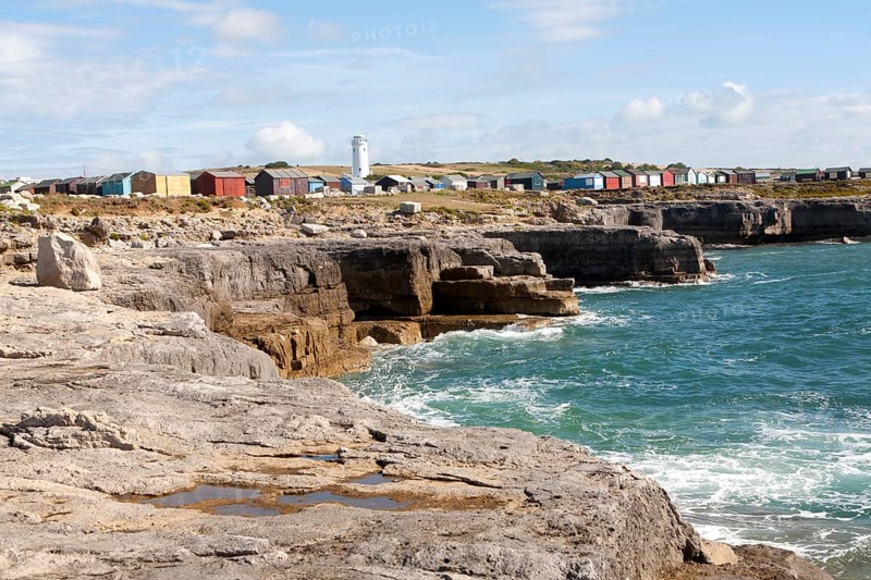 Old white lighthouse now a bird observatory and beach huts on the coast at Portland Bill, Isle of Portland, Dorset, England, United Kingdom, Europe