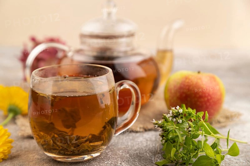 Red tea with herbs in glass teapot on brown concrete background and linen textile. Healthy drink concept. Side view, close up, selective focus