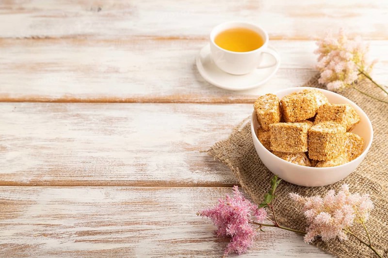 Traditional turkish delight (rahat lokum) in white ceramic plate with cup of green tea on a white wooden background. side view, copy space