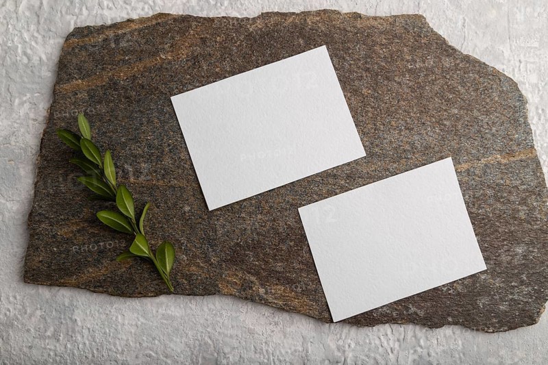 White paper business card, mockup with natural stone and boxwood branch on gray concrete background. Blank, flat lay, top view, still life, copy space