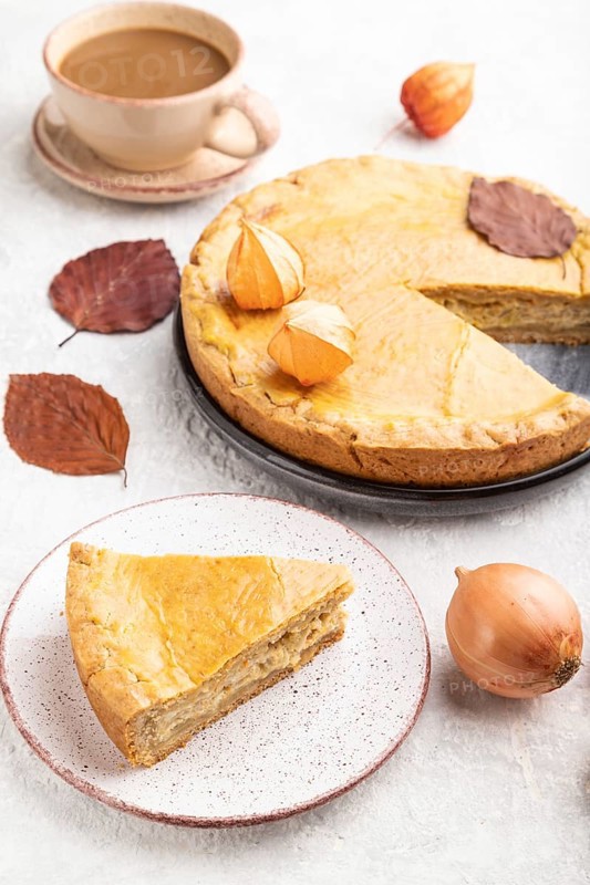 Autumn onion pie decorated with leaves and cup of coffee on gray concrete background. Side view, close up
