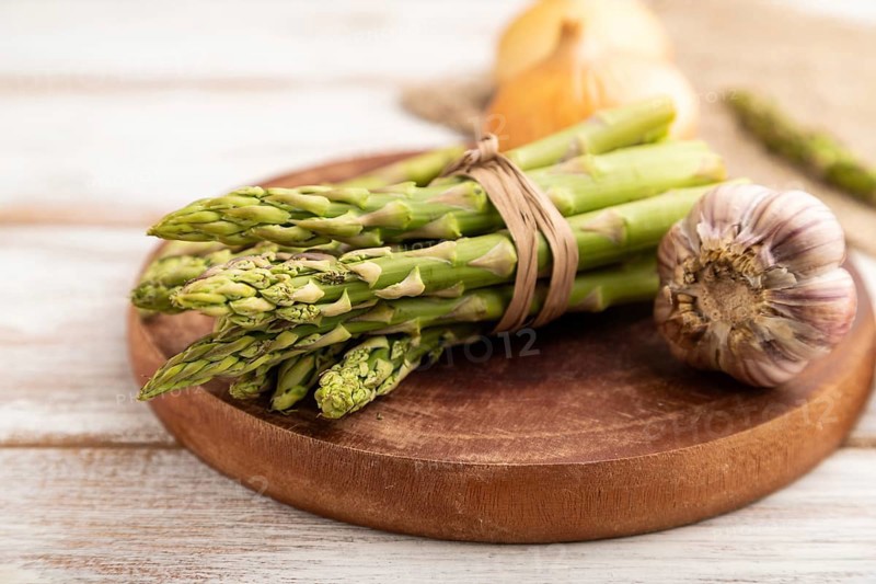 Bunch of fresh green asparagus, garlic, onion on white wooden background. Side view, selective focus. harvest, healthy, vegan food, concept