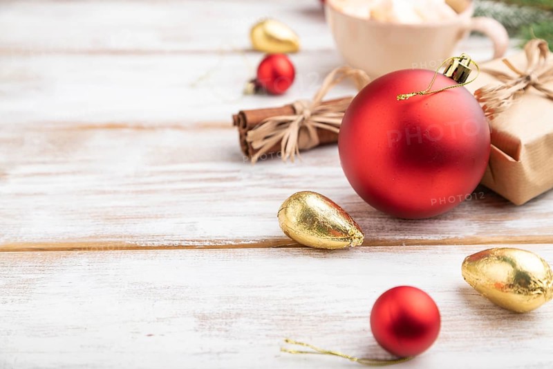 Christmas or New Year composition. Decorations, box, red balls, cinnamon, fir and spruce branches, cup of coffee, on a white wooden background. Side view, copy space, selective focus