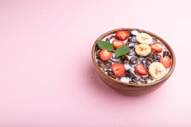 Chocolate cornflakes with milk and strawberry in wooden bowl on pink pastel background. Side view, copy space
