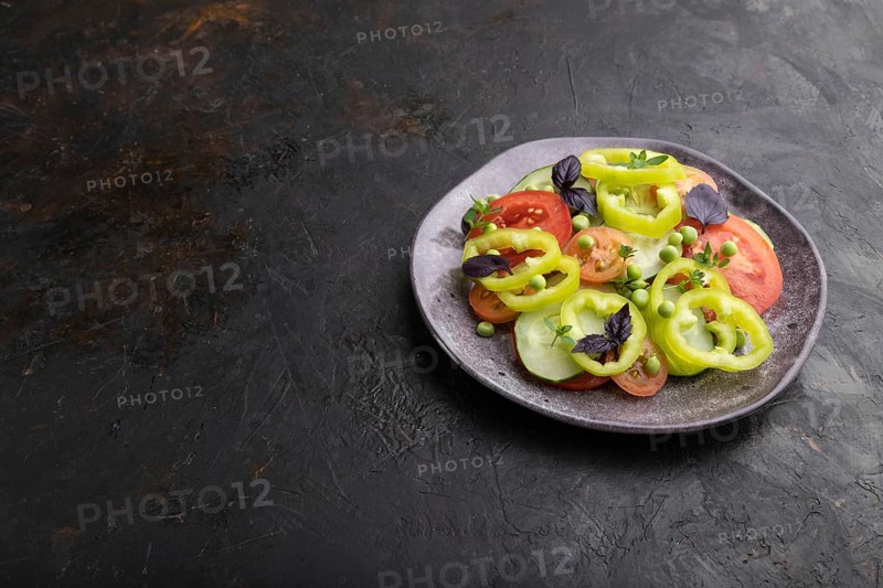 Vegetarian salad from green pea, tomatoes, pepper and basil on a black concrete background. Side view, copy space, close up