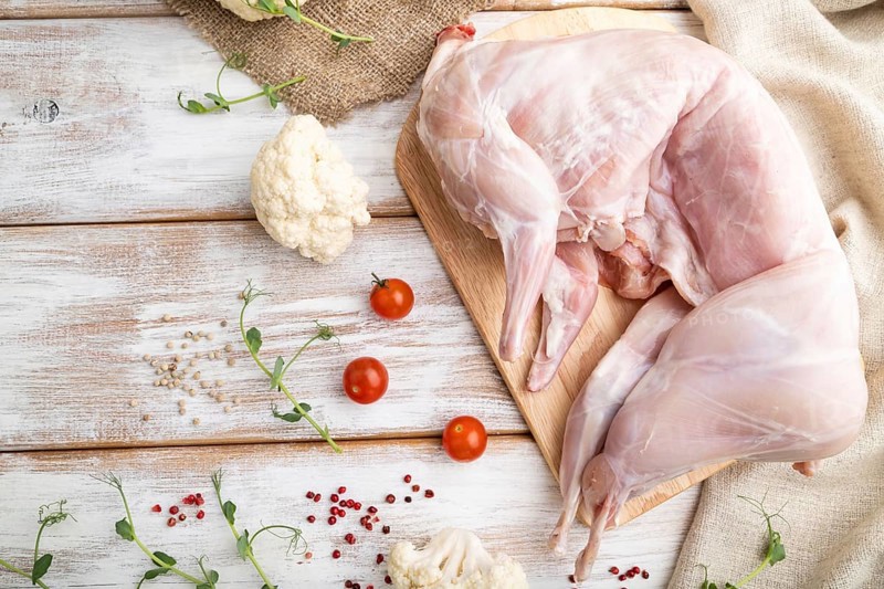 Whole raw rabbit with cauliflower, tomatoes and spices on a white wooden background and linen textile. Top view, flat lay, close up