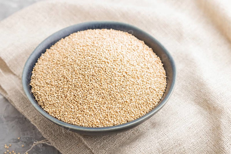 Blue ceramic bowl with raw white quinoa seeds on a gray concrete background and linen textile. Side view, close up, selective focus