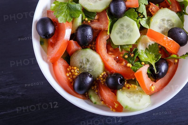 Vegetarian salad of tomatoes, cucumbers, parsley, olives and mustard on black wooden background, close up, selective focus