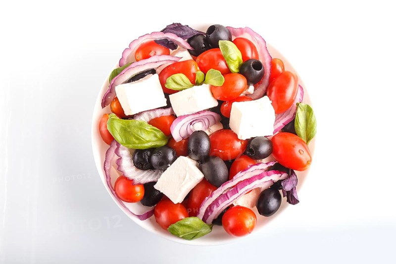 Greek salad with fresh cherry tomatoes, feta cheese, black olives, basil and onion isolated on white background. top view