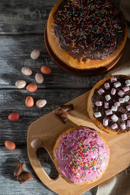 Homemade glazed and decorated easter pies with chocolate eggs and rabbits on a gray wooden background and linen textile. Hard light, contrast, top view, flat lay, close up