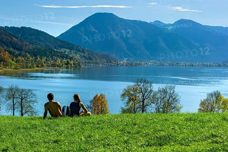 Tegernsee with Wallberg, couple sitting on a green meadow and looking at the lake, trees silhouetted on the shore, Mangfall mountains, Bavarian Alps, Alps, Upper Bavaria, Bavaria, Germany, Europe