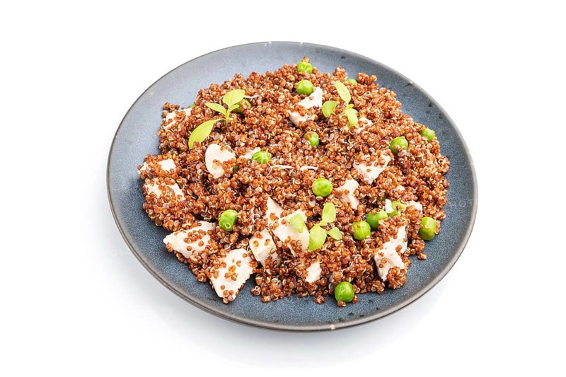 Quinoa porridge with green pea and chicken on ceramic plate isolated on white background. Side view, close up