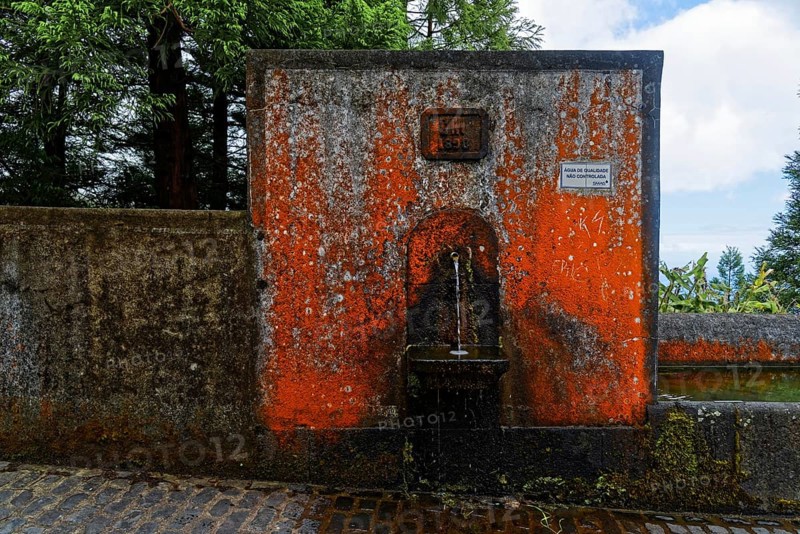 An old stone fountain with moss and algae growth and a weathered historical inscription, crater circular hiking trail, Caldeira das Sete Cidades, Muro das Nove Janelas, Sao Miguel, Portugal, Europe