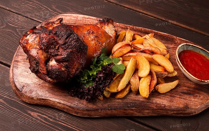Pork knuckle, in soy-honey sauce, with fried potatoes, on a wooden chopping board, homemade, no people