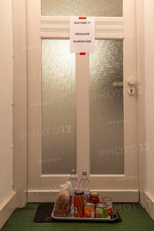 Symbolic image Domestic quarantine, man is in isolation at home due to a suspected corona infection, warning sign for visitors on the front door, communicating with a visitor through the door, neighbours have placed food in front of the door