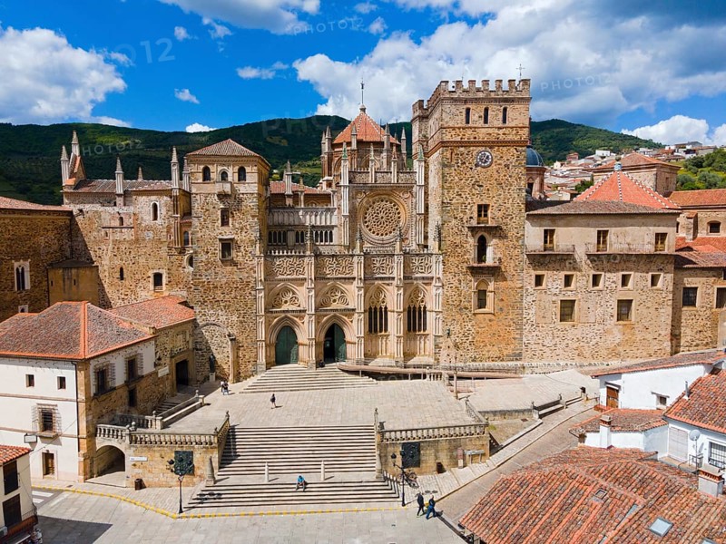 Aerial view of the facade of a monastery with red roofs and wide stairs under a blue sky in Spain. Historical architecture is presented, aerial view, pilgrimage church and monastery, Real Monasterio de Nuestra Señora de Guadalupe, Guadalupe, Cáceres province, Caceres, Extremadura, Spain, Europe